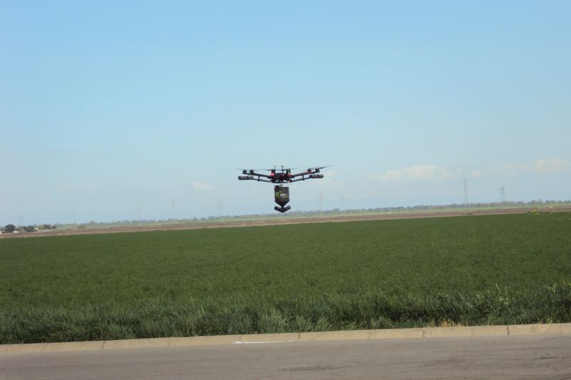 Spray drone flying above a flat green field during an aerial pesticide application training day
